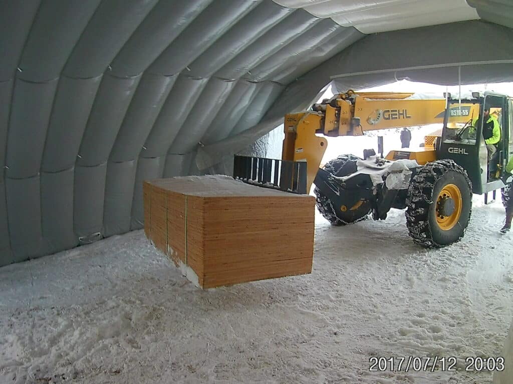Telehandler stacking packaged building materials inside a Njordair Fast Tent in Montana